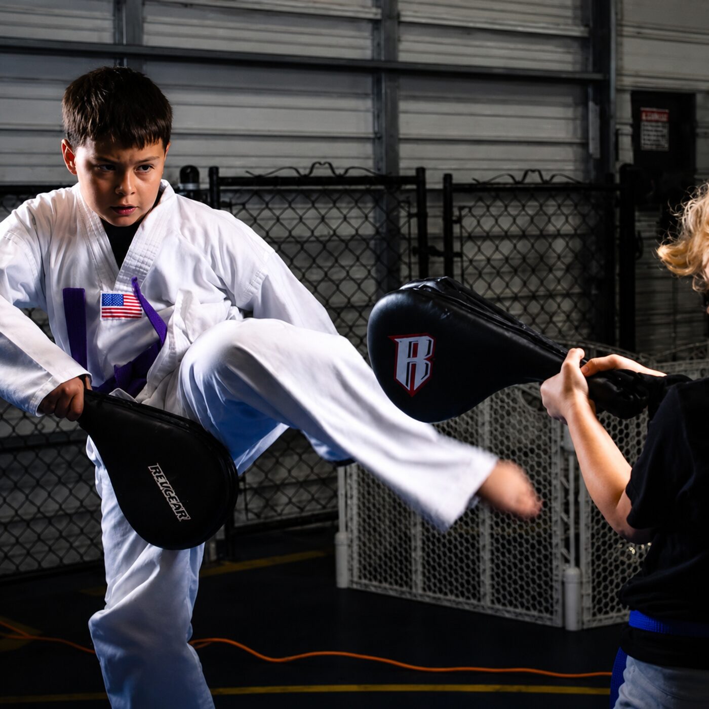 Young student landing a front kick on a training pad during youth martial arts class at Sud'n Impact in Fort Wayne, Indiana
